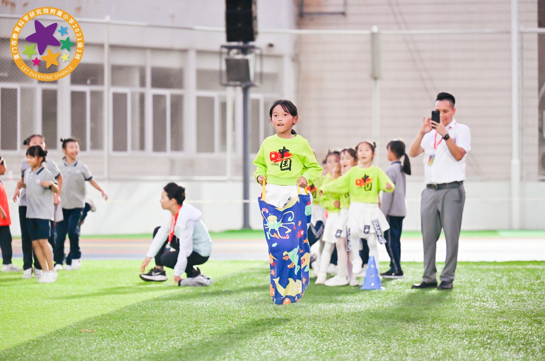 女孩穿统一活动服参加袋鼠跳或套袋竞赛，多人在运动场