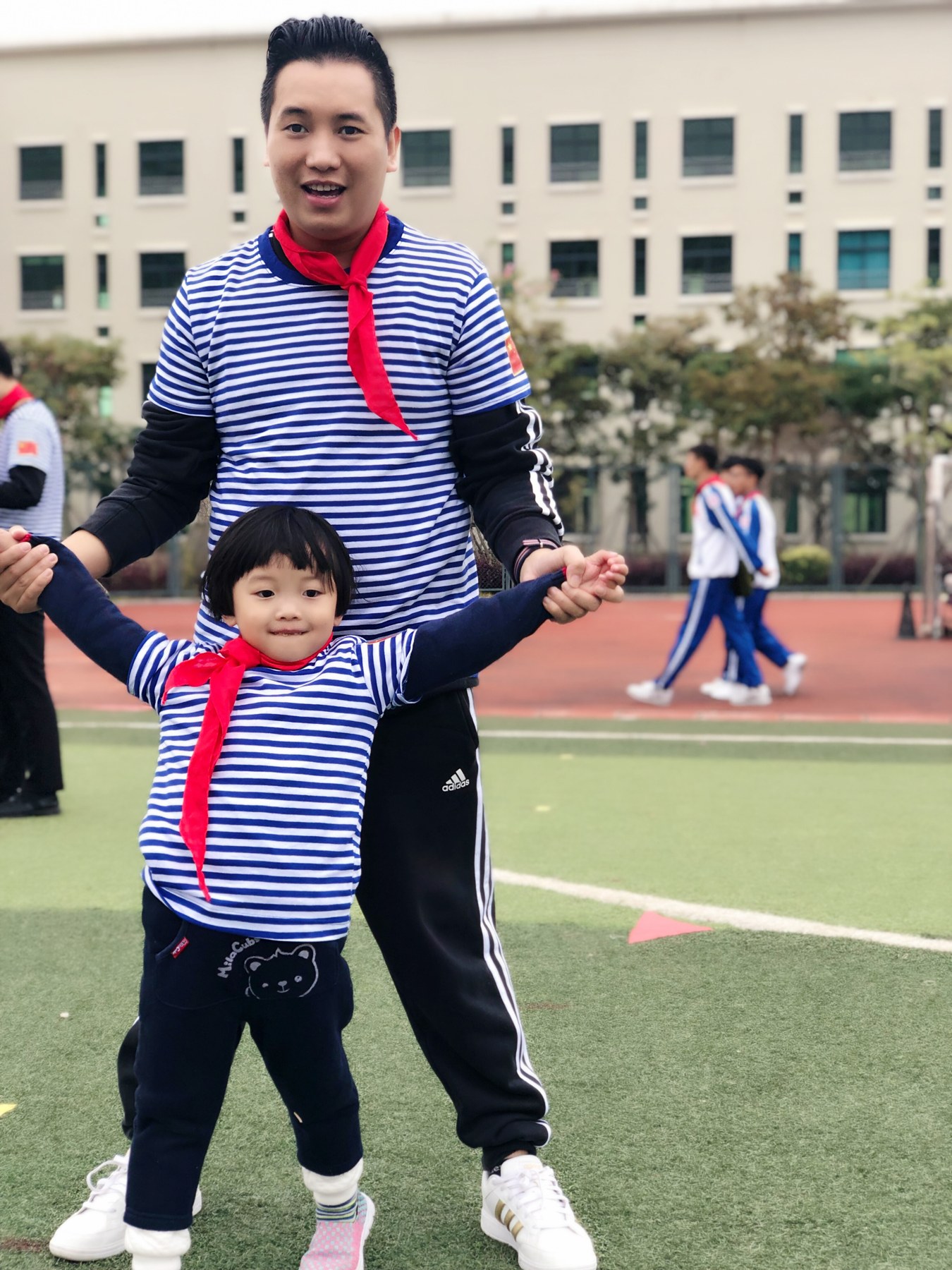 成年男性牵着幼儿站在运动场上