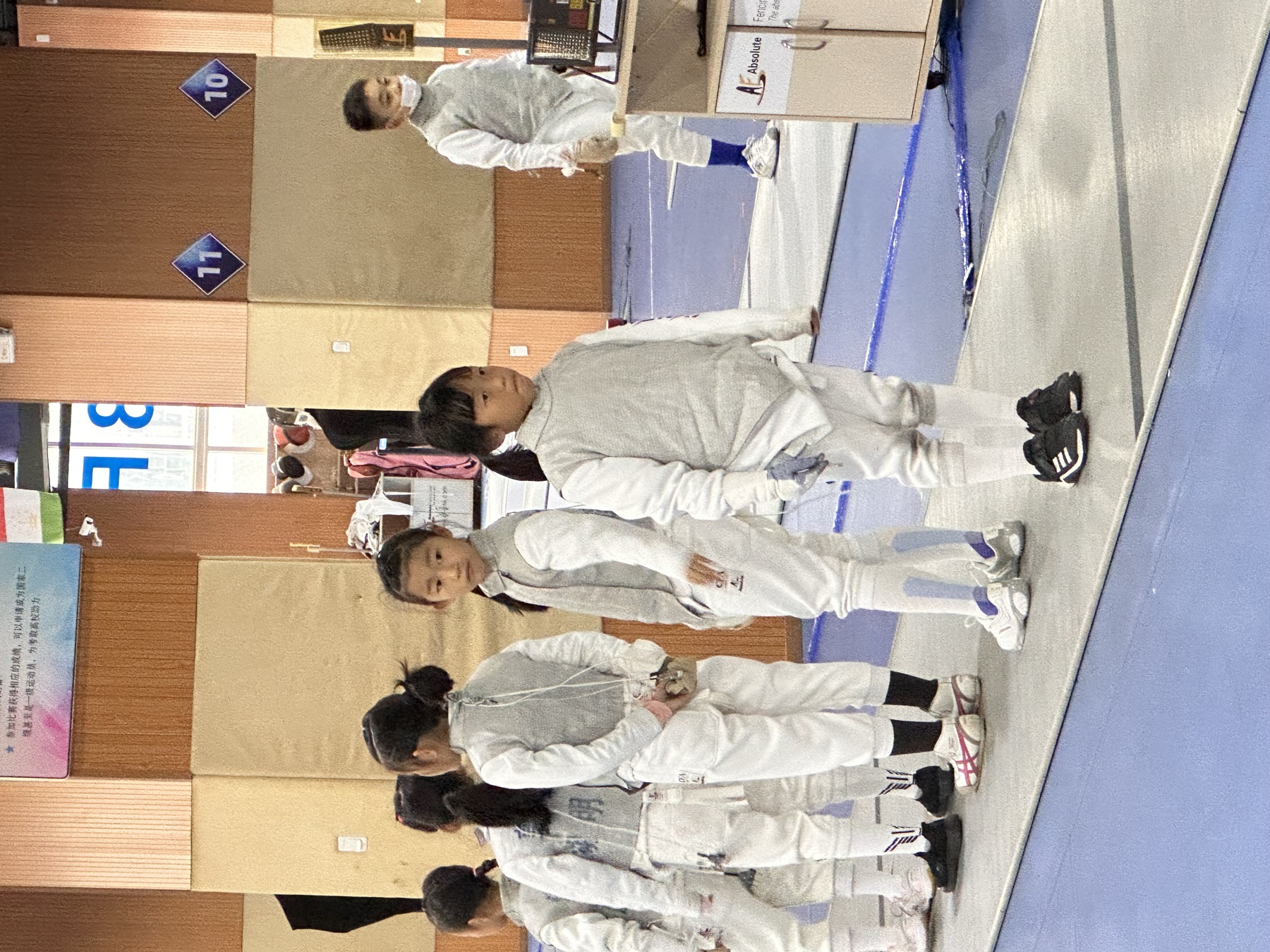 女孩穿击剑服在训练或比赛场地与其他儿童列队